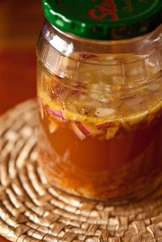 a glass jar filled with liquid sitting on top of a woven place mat next to a green lid