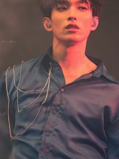 a young man with black hair wearing a blue shirt and silver chain around his neck