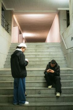 two men are sitting on the stairs looking at their cell phones in front of them