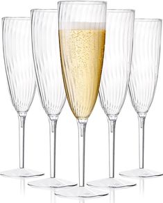 four wine glasses are lined up next to each other on a white surface, one is filled with champagne