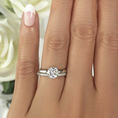 a woman's hand with a diamond ring on it and flowers in the background