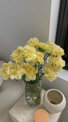 yellow flowers are in a vase on a white table next to a small round object