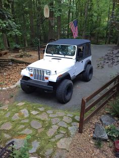 a white jeep with an american flag on the roof is parked in front of a wooded area