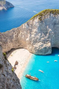 an aerial view of boats in the water near a rocky cliff and beach with blue water