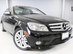 a black mercedes c - class car is parked in a showroom with white walls