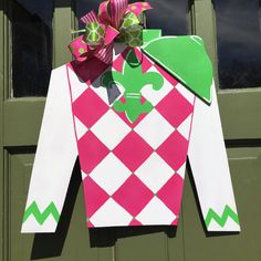 a pink and green argyle sweater hanging from a door with a bow on it's head