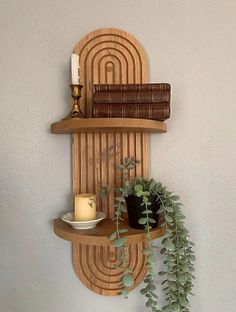 a wooden shelf with some plants on it and a candle next to it in front of a white wall