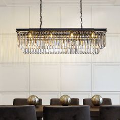 a chandelier hanging over a dining room table with black chairs and gold balls