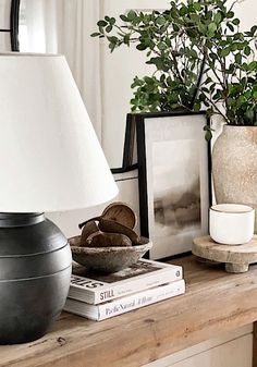 a table topped with books and a lamp next to a potted plant on top of a wooden table