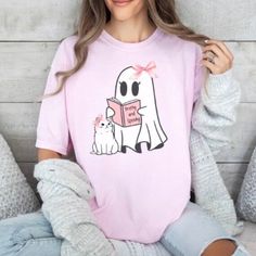 Comfort Colors® Coquette Shirt, Coquette Halloween Crewneck, Cute Ghost, Pink Bow, Cute Cat, Reading a Book Sweatshirt, Womens Spooky Season  🎀This design features a very girly ghost wearing a pink bow. Her cat is at her feet and is wearing a matching pink bow! The ghost loves to read and she is reading a book titled Pretty and Spooky 💖The Comfort Colors® tee is knit in one piece using tubular knit, which reduces fabric waste and makes the garment more attractive.  The garment is sewn around t Playful Crew Neck Tops For Halloween, Pink Tops With Cartoon Print For Fall, Pink Cartoon Print Tops For Fall, Kawaii Letter Print Tops For Fall, Hello Kitty Print Crew Neck Tops For Fall, Cute White Tops For Halloween, Kawaii Graphic Print Tops For Fall, Kawaii Tops With Graphic Print For Fall, Cute Halloween Tops With Character Print