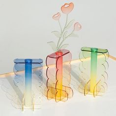 three colorful vases with flowers in them sitting on a white surface, next to each other