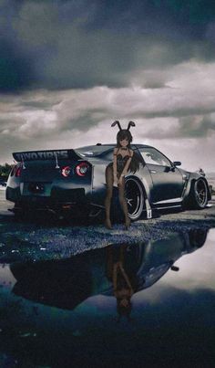 a woman is standing next to a car with horns on it's head and her reflection in the water