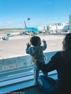 a woman holding a child looking out an airport window