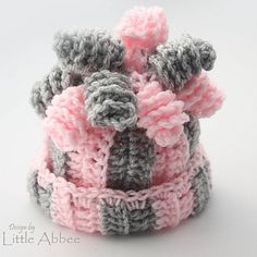 a crocheted pink and gray hat with pom poms