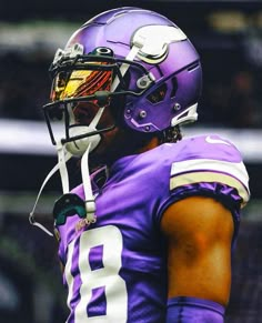 a close up of a football player wearing a purple uniform and holding a helmet on his head