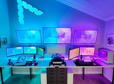 there are many computer screens on the desk in this room with purple lights and blue lighting