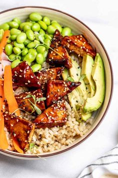 a bowl filled with rice, vegetables and tofu next to sliced avocado