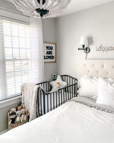 a white bed sitting in a bedroom next to a window with blinds on the windowsill