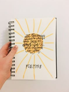 a hand holding a spiral notebook with writing on the cover and sunburst above it