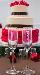 two wine glasses sitting on top of a table next to a cake with red roses