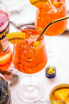 two glasses filled with different types of drinks and garnished with orange peels