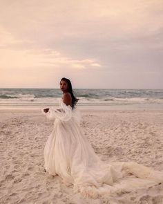 a woman standing on top of a sandy beach next to the ocean wearing a white dress