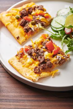 two slices of pizza on a white plate next to a salad and cucumber