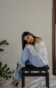 a woman sitting on top of a black chair next to a mirror and potted plant