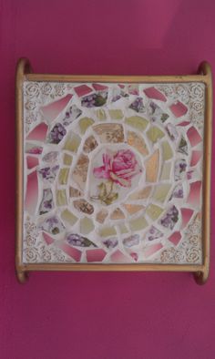 a pink rose sits in the center of a mosaic tile wall hanging on a purple wall