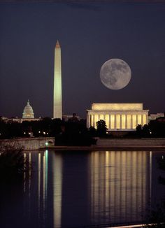 the washington monument is lit up at night with the moon in the sky above it