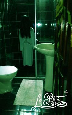 a woman standing in a bathroom next to a white toilet and sink with black tile on the floor