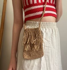 a woman wearing a red and white top holding a straw bag with fringes on it