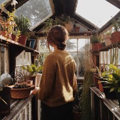 a woman standing in a greenhouse looking at potted plants and other houseplants