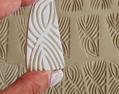 a hand holding a piece of white tile in front of a textured wallpaper