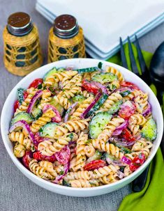 a pasta salad with cucumbers, tomatoes and red onions in a white bowl