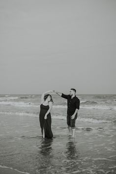 a man and woman standing in the ocean holding each other's hands with their arms