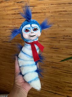 a hand holding a stuffed animal that looks like a caterpillar with blue hair