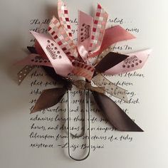 a pink and brown pinwheel with ribbon on it's side sitting on top of a piece of paper