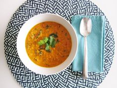 a white bowl filled with soup on top of a blue and white place mat next to a silver spoon