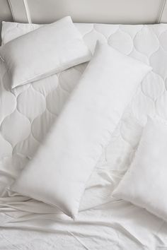 four pillows on top of an unmade bed with white sheets and pillowcases