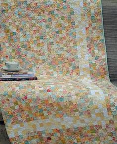 a couch with a quilt on top of it next to a coffee cup and books