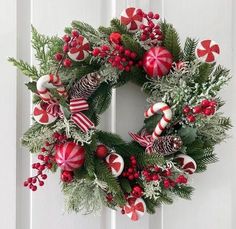 a wreath with candy canes, holly and pine cones is hanging on the door