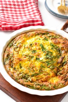 an omelet with spinach and cheese in a white dish on a wooden board