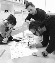 two men and a woman looking at blueprints on the floor in an office