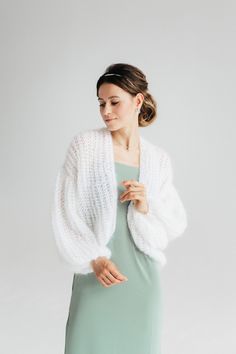 a woman in a green dress is wearing a white knitted cardigan with long sleeves