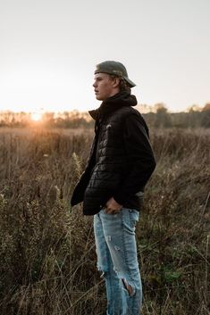 a man standing in the middle of a field with his hands in his pockets and looking off into the distance