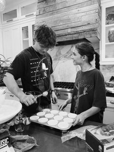 two people in the kitchen making muffins on top of a pan and looking at each other