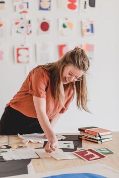 a woman in an orange shirt and black skirt working on some art work at a table