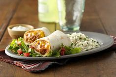 a burrito on a plate with rice and lettuce next to a glass of water