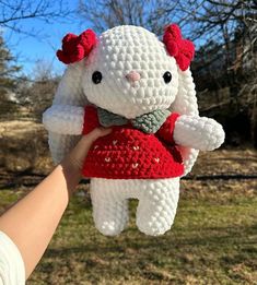 a hand holding a small white crocheted stuffed animal in a red dress and bow